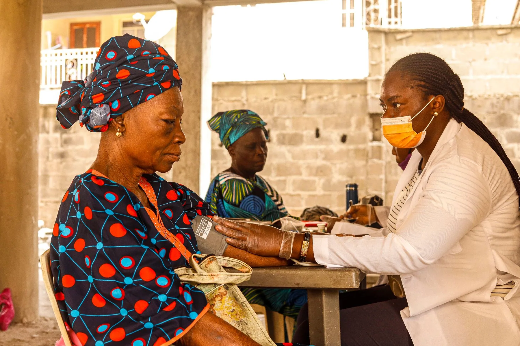 African healthcare professional checking an older woman's blood pressure